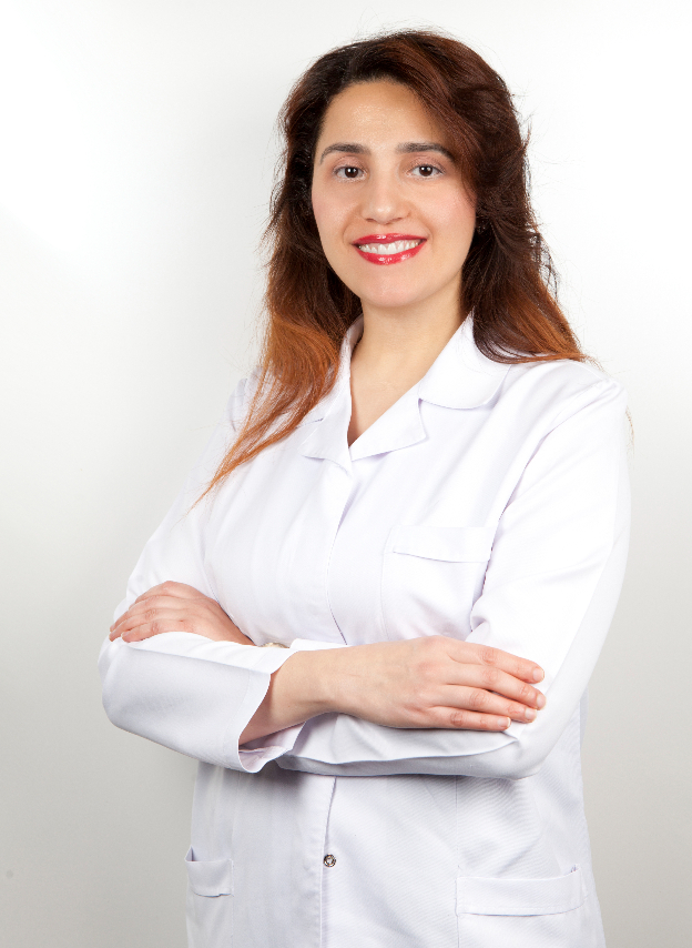 Eine junge Frau mit langen braunen Haaren lächelt freundlich im weißen Arztkittel